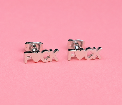 Silver 'F*ck' earrings on a pink background
