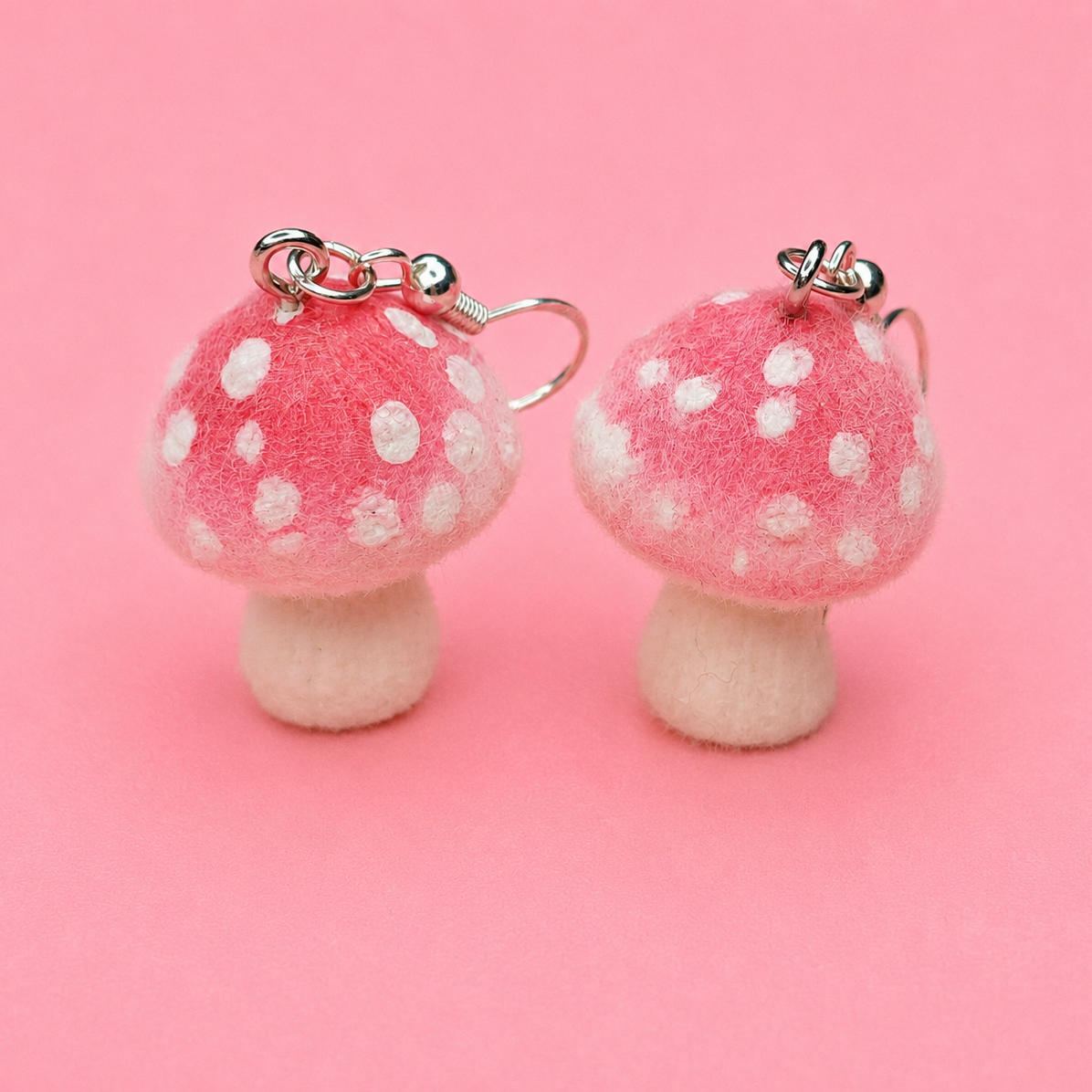 Pair of pink mushroom earrings with white spots on a pink background
