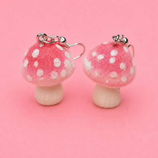 Pair of pink mushroom earrings with white spots on a pink background