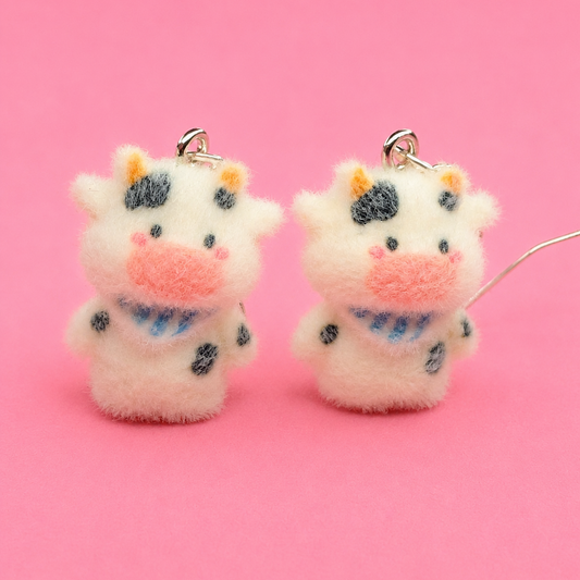 Two fluffy cow-shaped keychains with a pink background