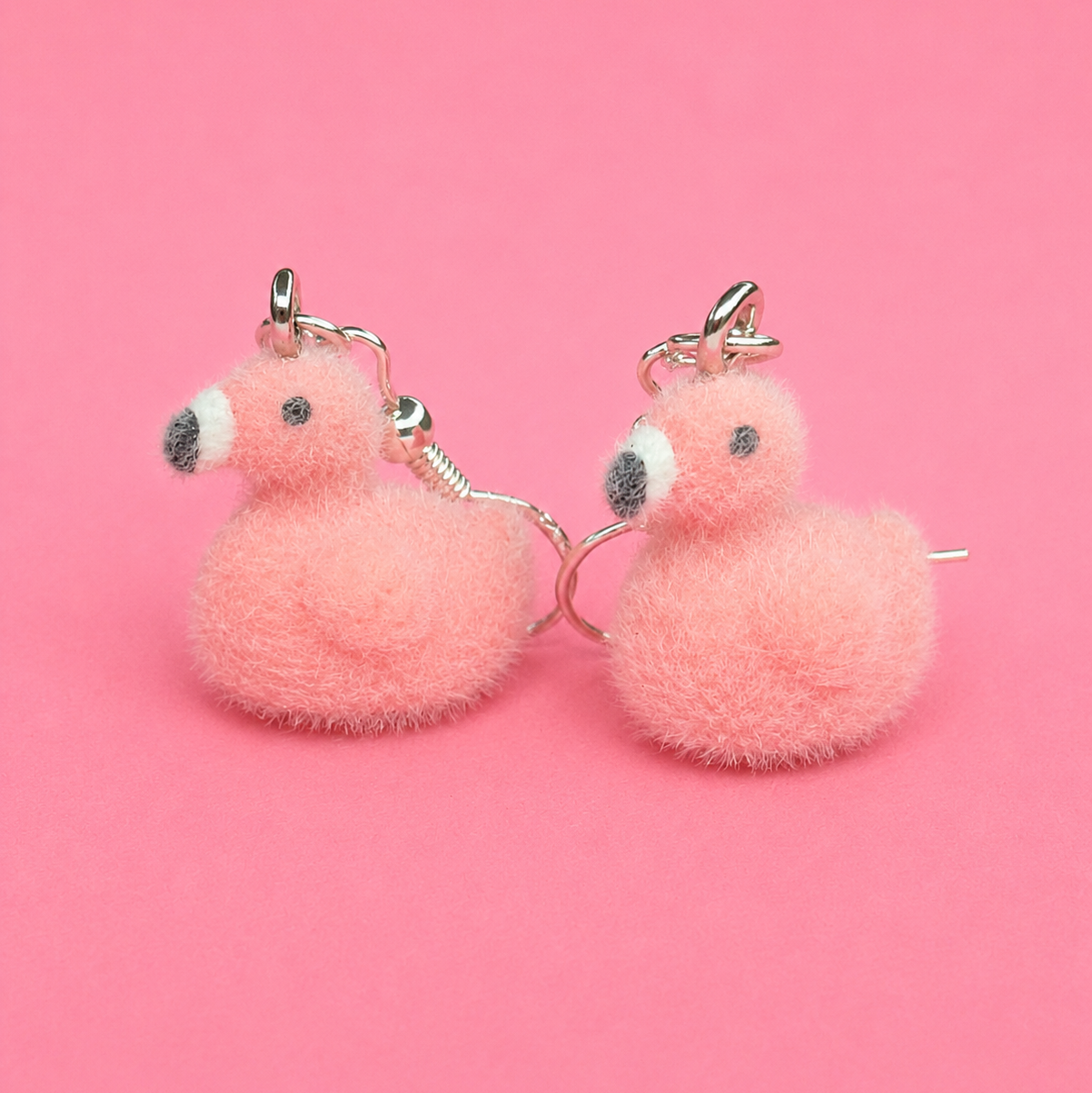 Pair of pink fluffy duck-shaped earrings on a pink background